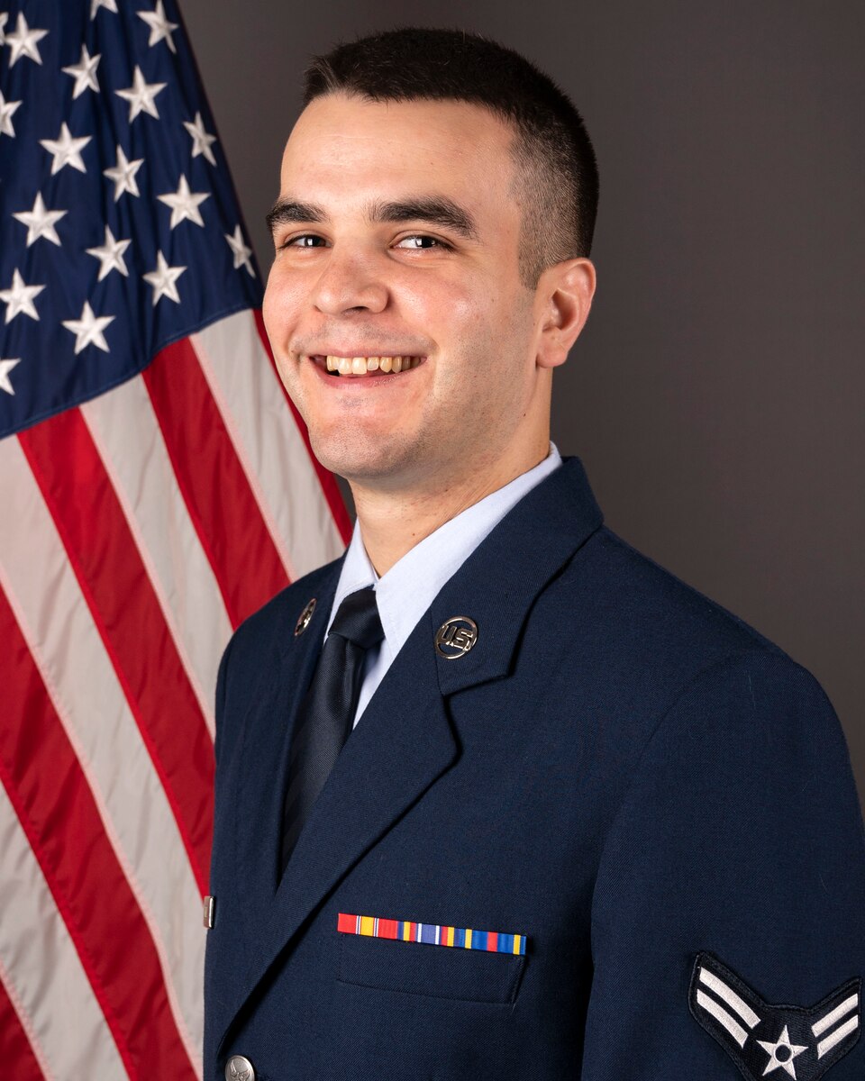Official headshot of A1C Daniel Gelman in front of the American flag. He is wearing the blue service dress uniform.