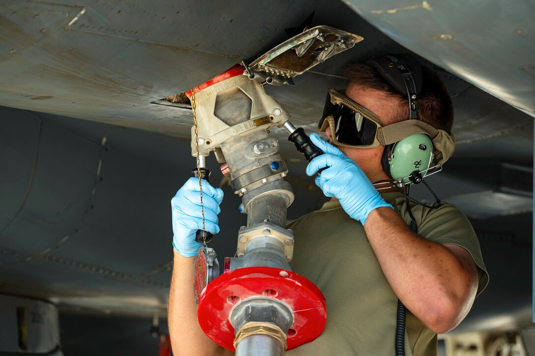 An airman wearing goggles attaches a fuel hose to an aircraft.