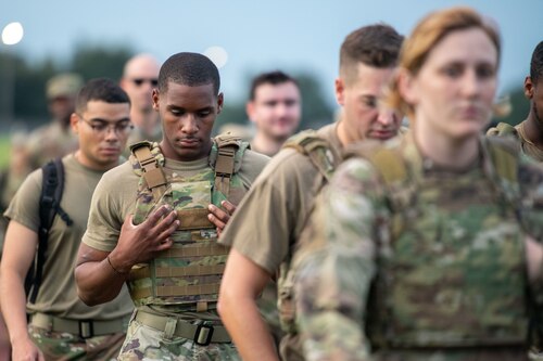 An Airman looks down and clings to the front of his ruck while marching among other Airmen
