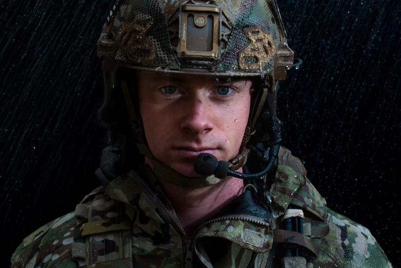 An Airmen looks directly at the camera as rain fall around him.