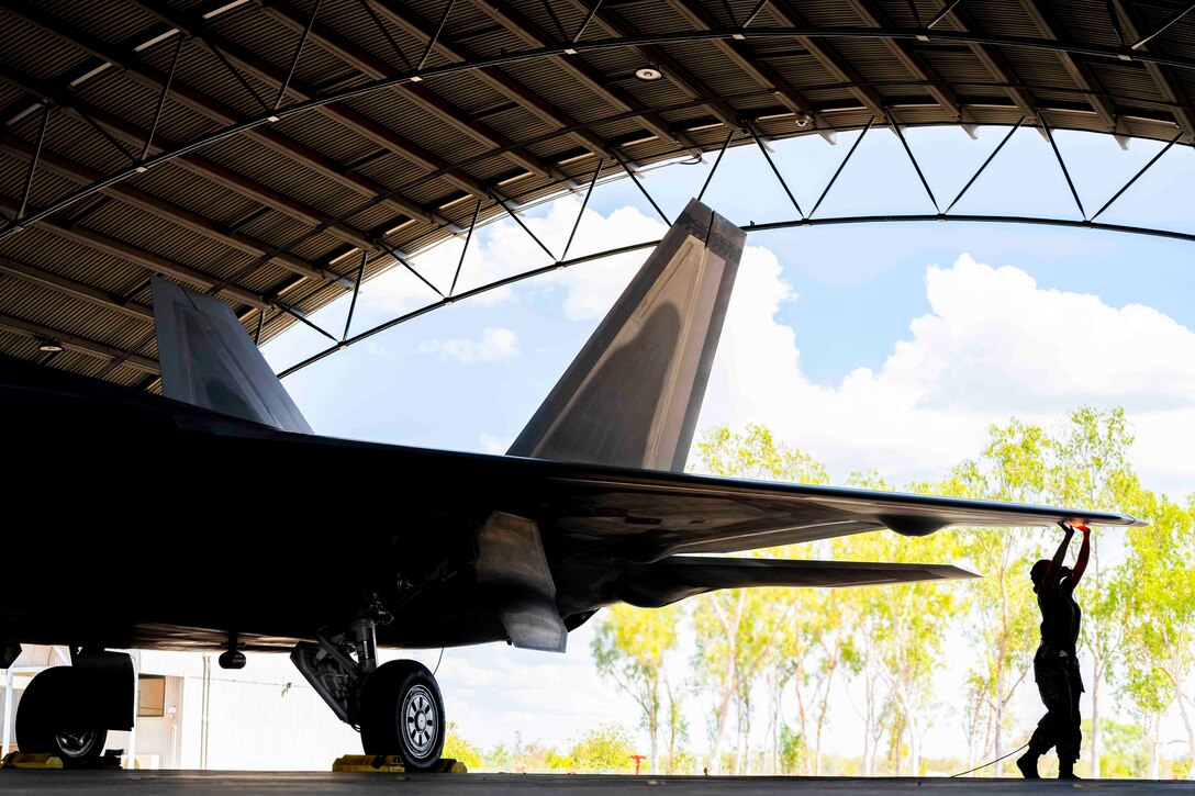 An airman shown in silhouette checks a parked aircraft’s wing.