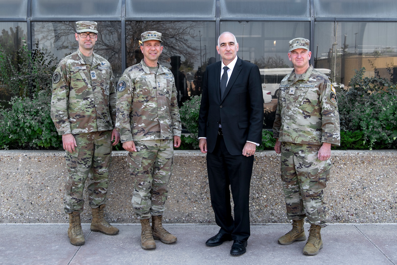 Four men, three in military uniforms and one in a suit, pose for a group photo