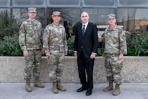 Four men, three in military uniforms and one in a suit, pose for a group photo