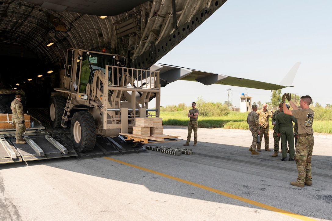Service members direct a vehicle backing into an open aircraft.