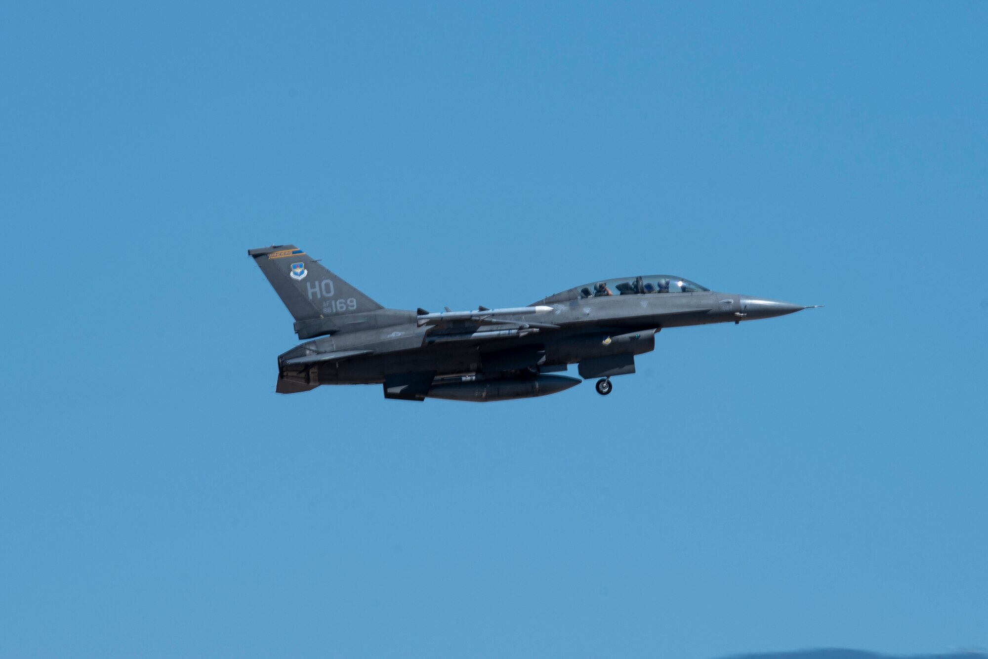 A grey F-16 Viper flies through the blue sky.