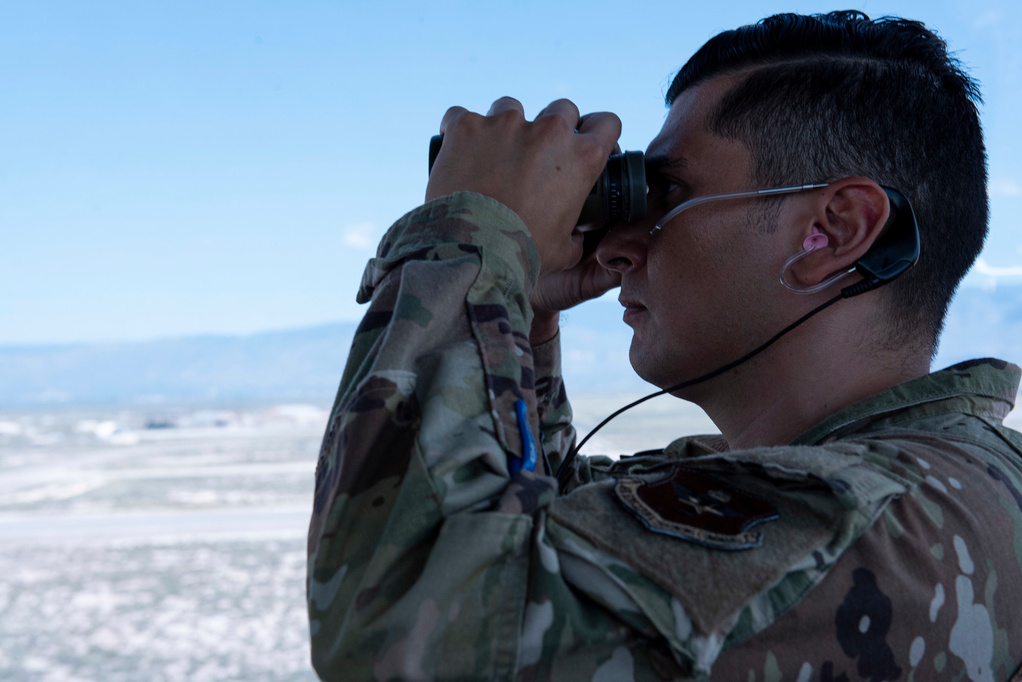 A person wearing green ocps uses a pear of black binoculars.