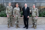 Four men, three in military uniforms and one in a suit, pose for a group photo