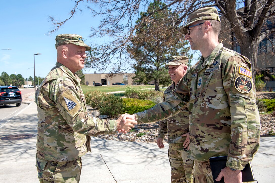 Three men in military uniforms greeting each other, two are shaking hands