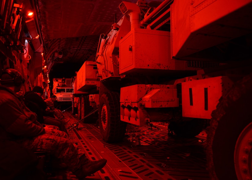 Large vehicles sit inside the back of an aircraft.