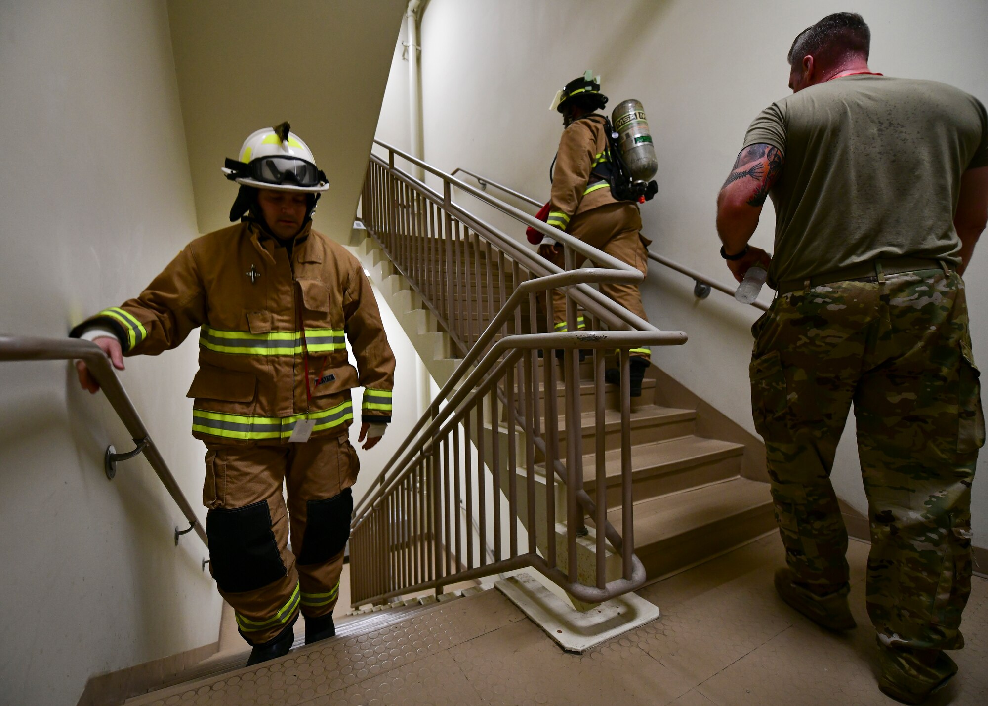 Military firefighters climb stairs in uniform.