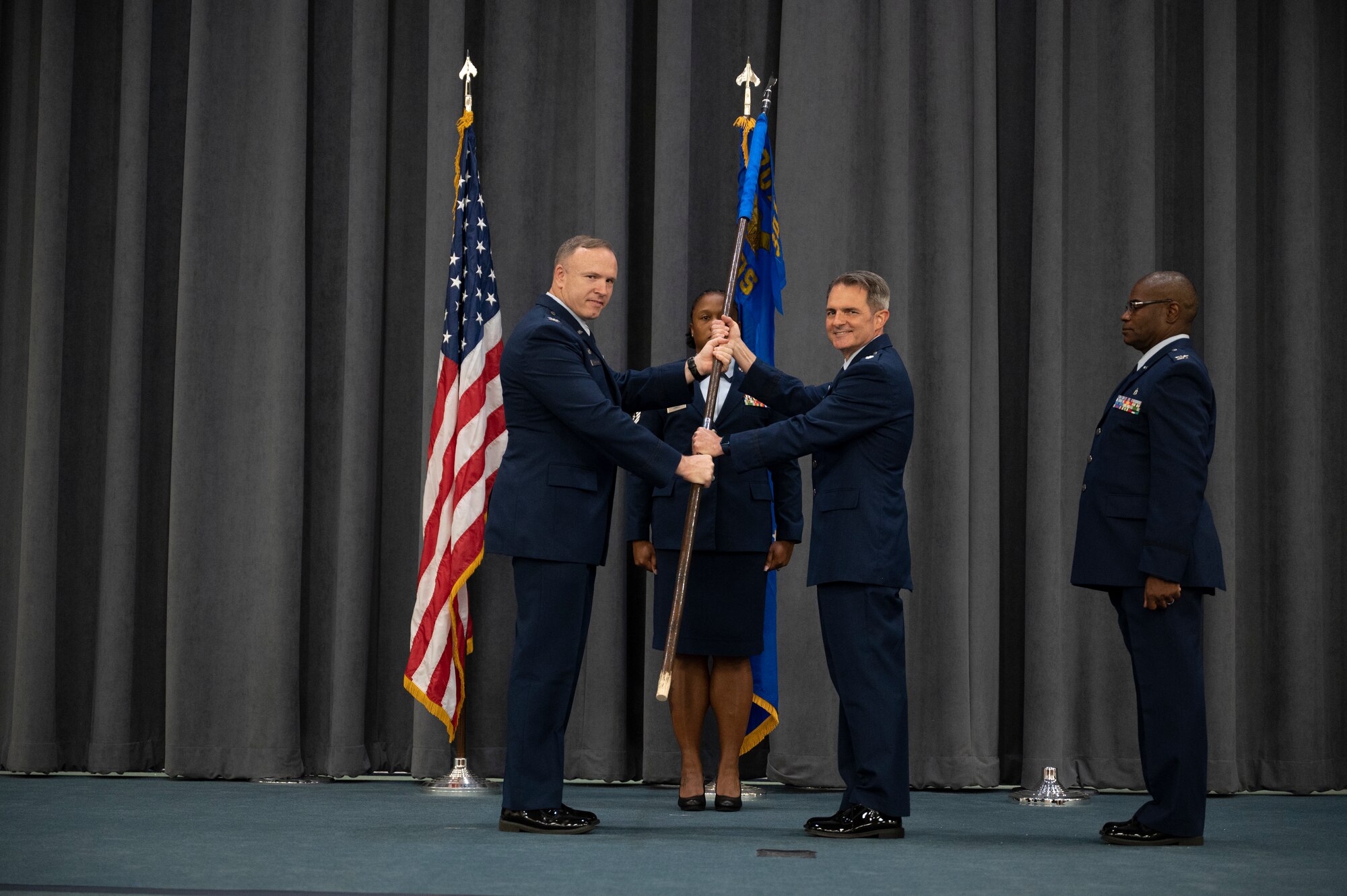 Two men exchange a flag while a woman and another man stand at attention.