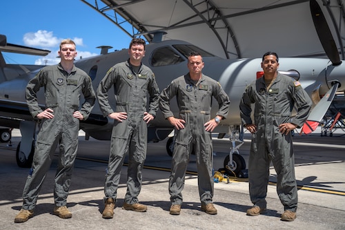 Four military members stand in front of a U-28 Draco aircraft.
