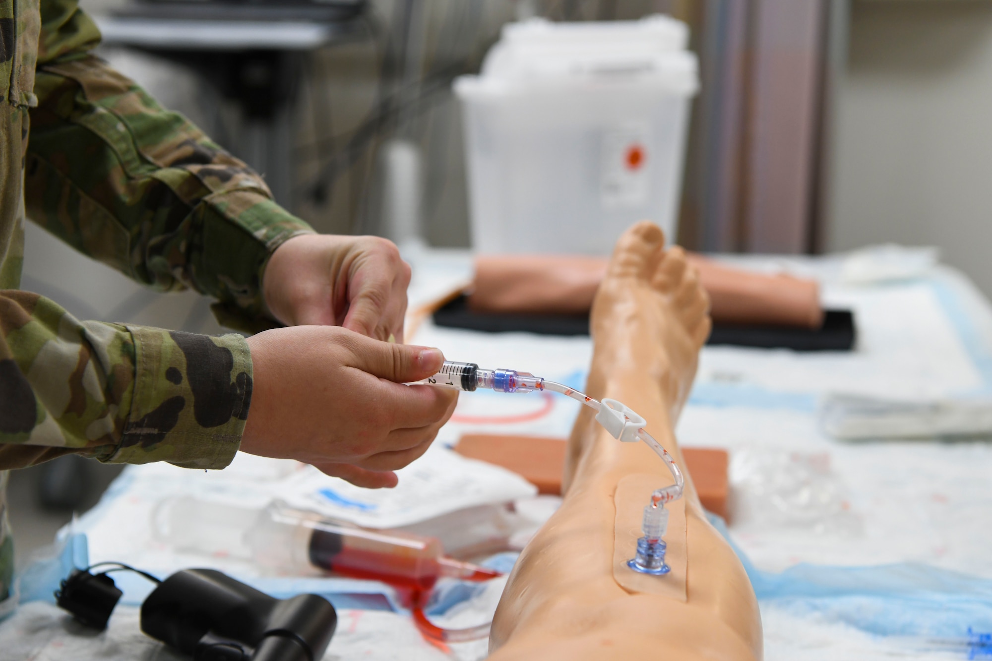 A U.S. Air Force Airman simulates a fluid infusion with an inner bone catheter in a training mannequin’s leg