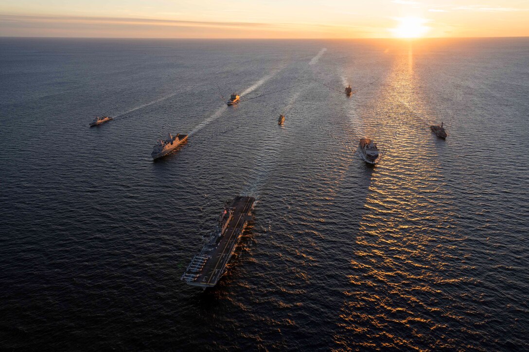 Ships sail in formation while the sun peeks over the horizon.