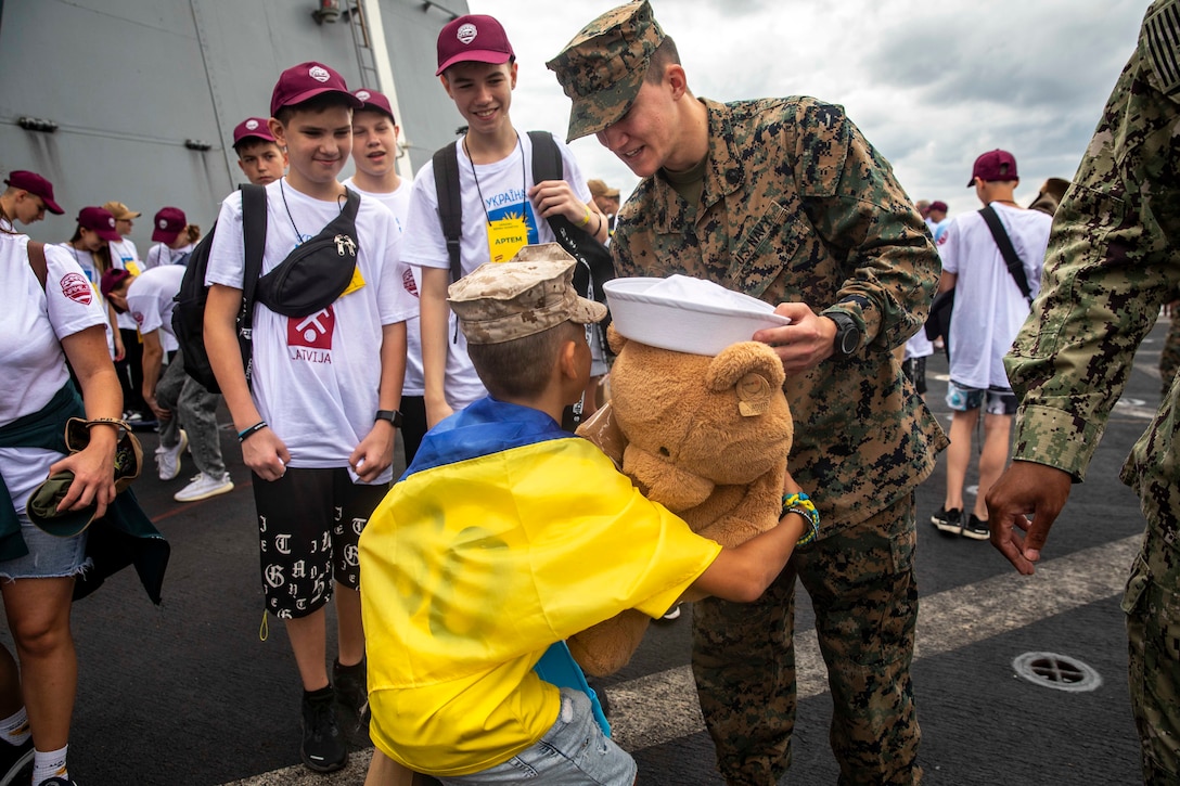 A sailor gives a stuffed animal to a Ukrainian child while other children look on