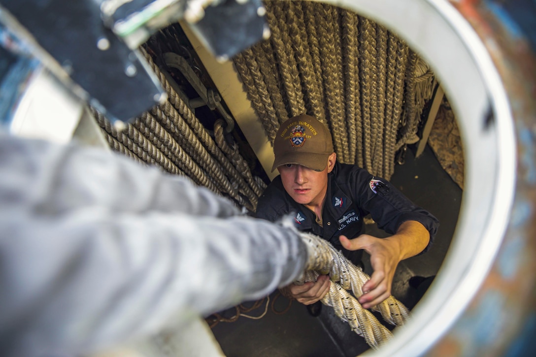 A sailor pulls on a rope aboard a ship as seen from above.