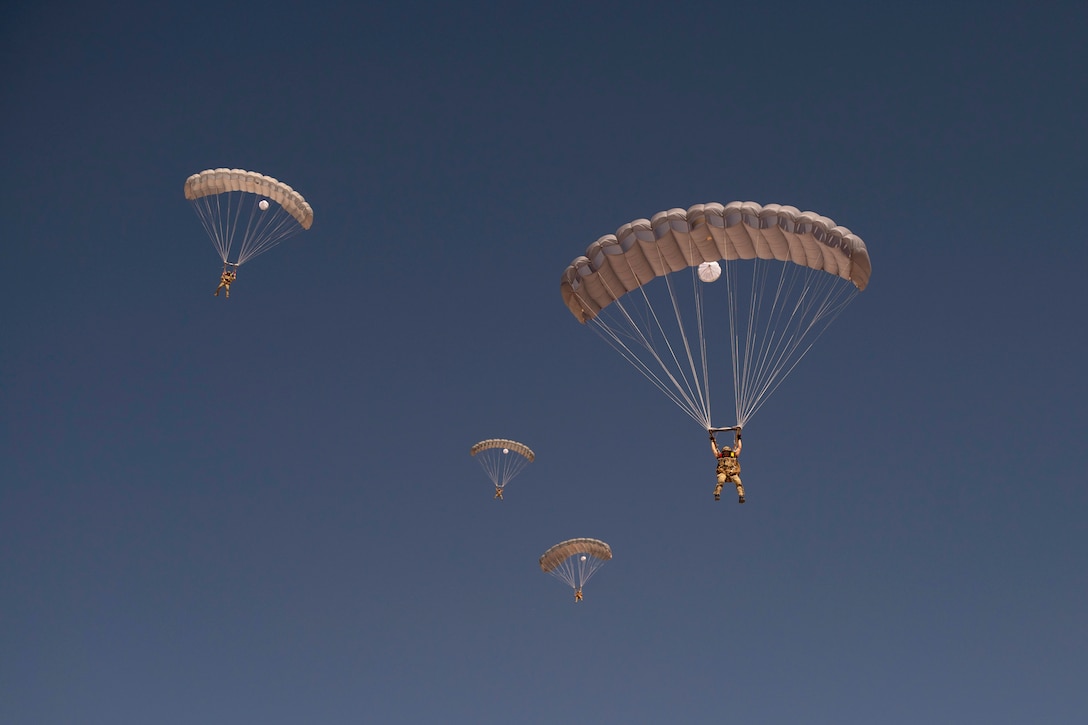 Four airmen free-fall with parachutes next to one another.