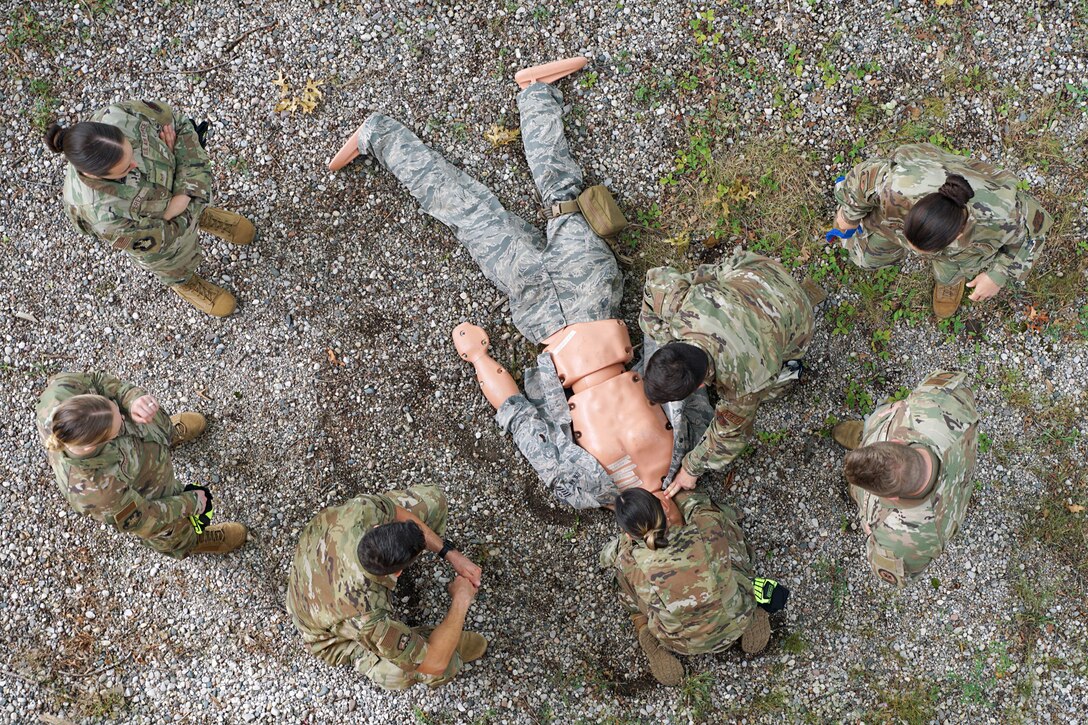 Two airmen check the pulse of a mannequin on gravel as fellow airmen watch during training.