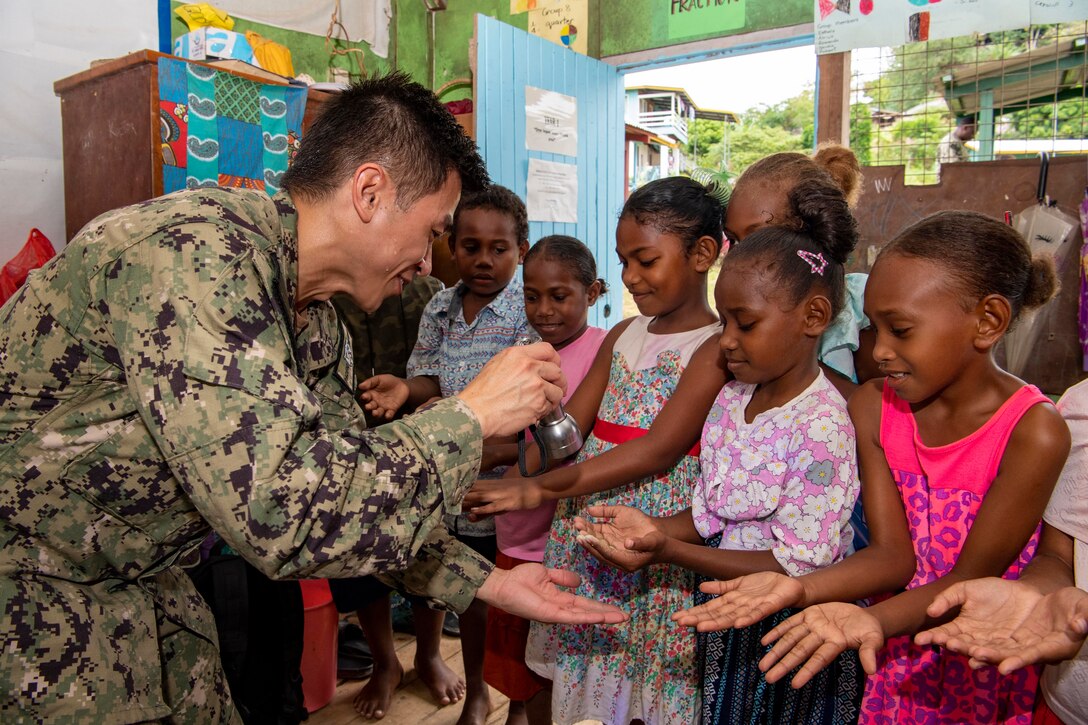 A sailor shines a flashlight on the hands of school children.