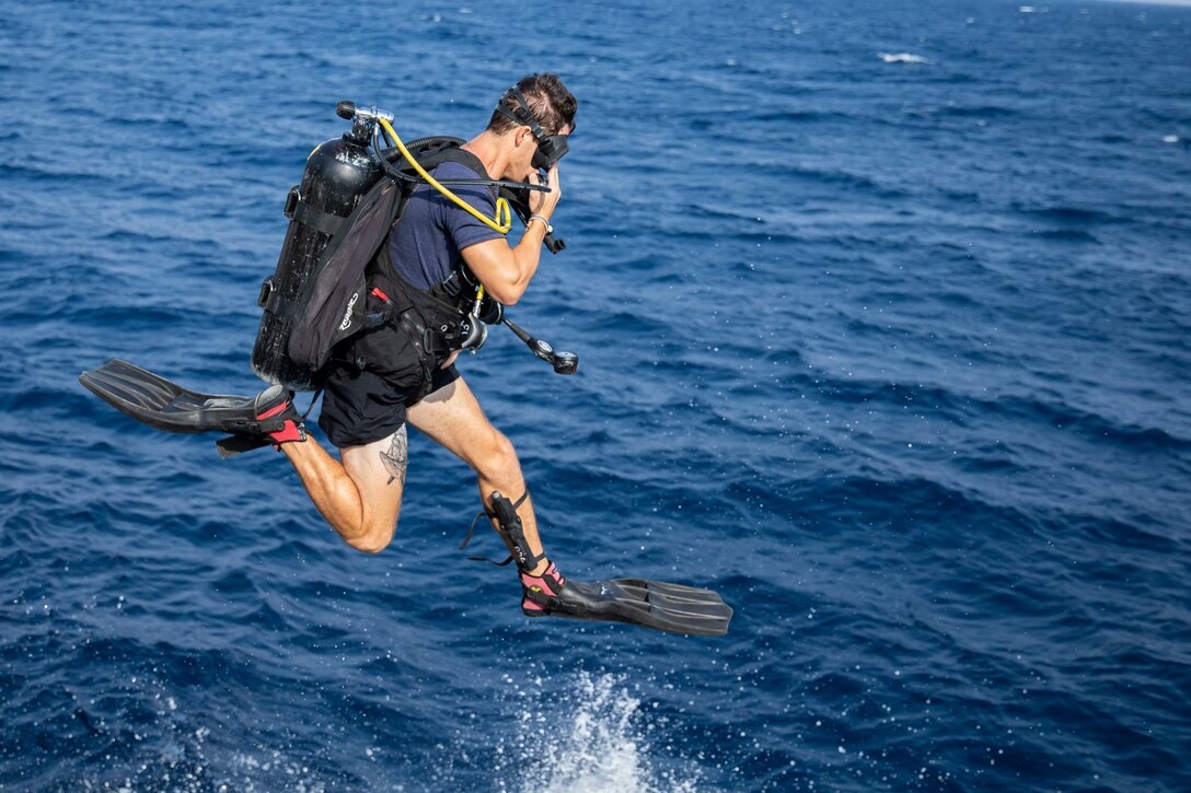 A sailor in diving gear jumps into the water.