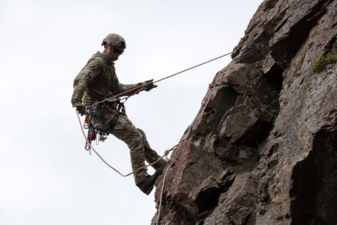 An airman rappels down the face of a cliff.
