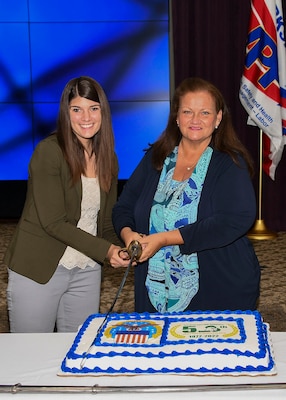 Two ladies cut a cake with a sword.