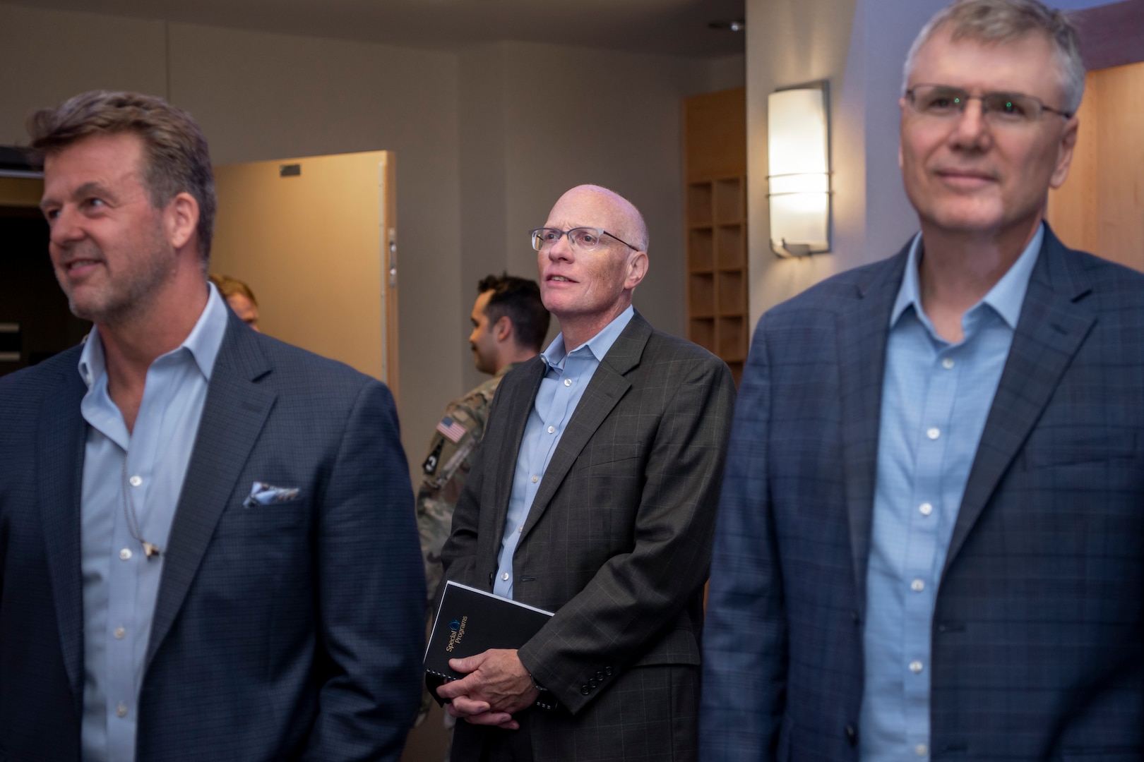 Three men in suits standing, listening to a briefing