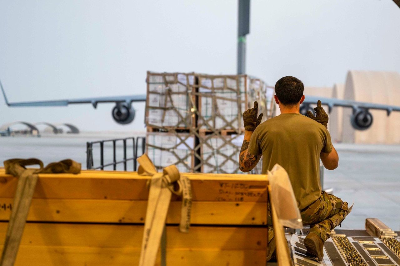 A service member signals toward a cargo pallet.