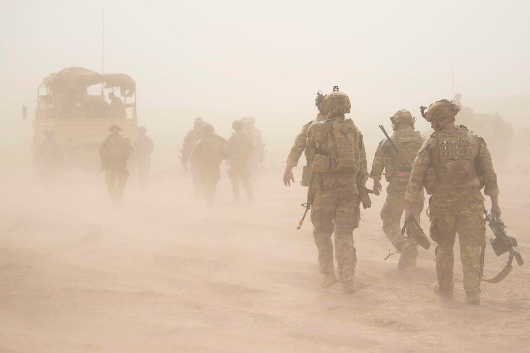 Guardsmen walk through a sandstorm toward a vehicle.