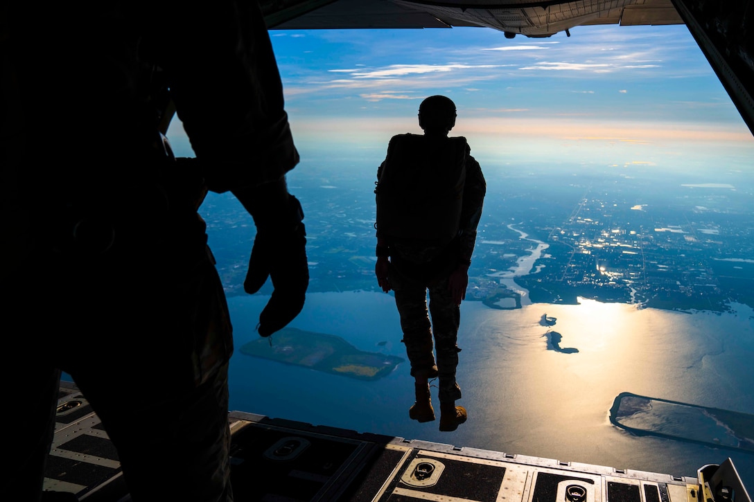 A soldier jumps from the back of an airborne aircraft.