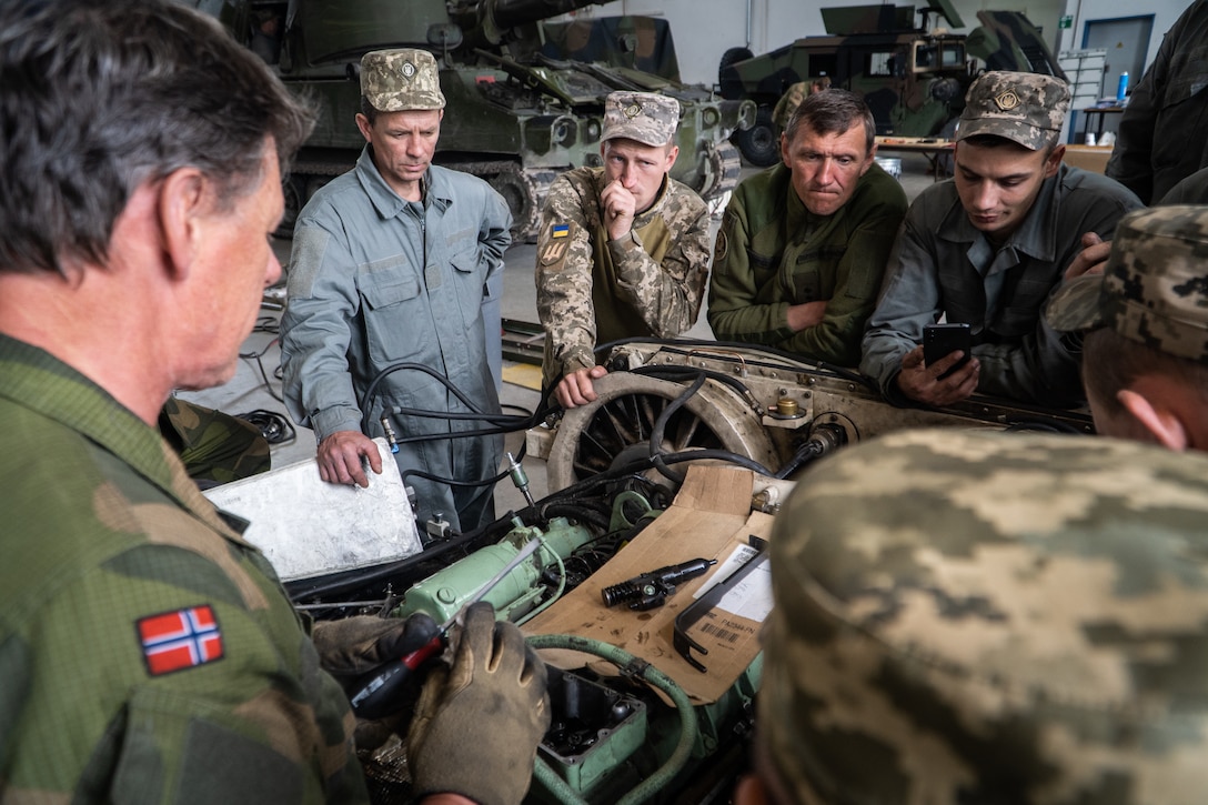 Soldiers examine the interior of an engine compartment.