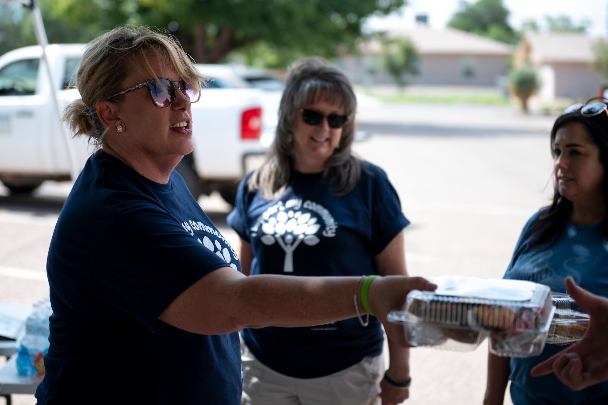 A woman in a blue t-shirt hands out a clear container of food to someone.