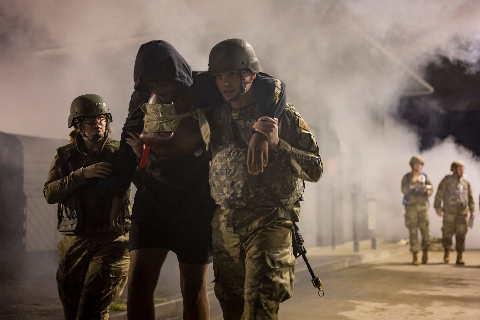 U.S. Air Force members carry a simulated victim with smoke in the background.