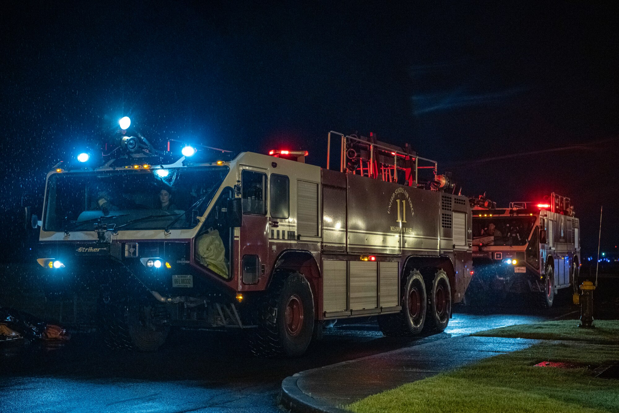 U.S. Air Force firefighters drive in fire trucks towards an incident scene.