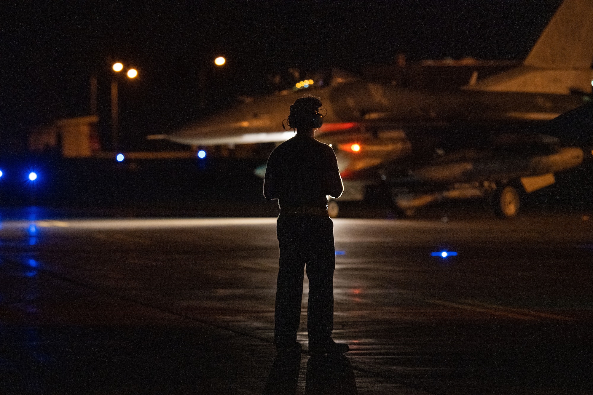 A U.S. Air Force member stands on the flight line silhouetted by the lights of an F-16 Fighting Falcon.