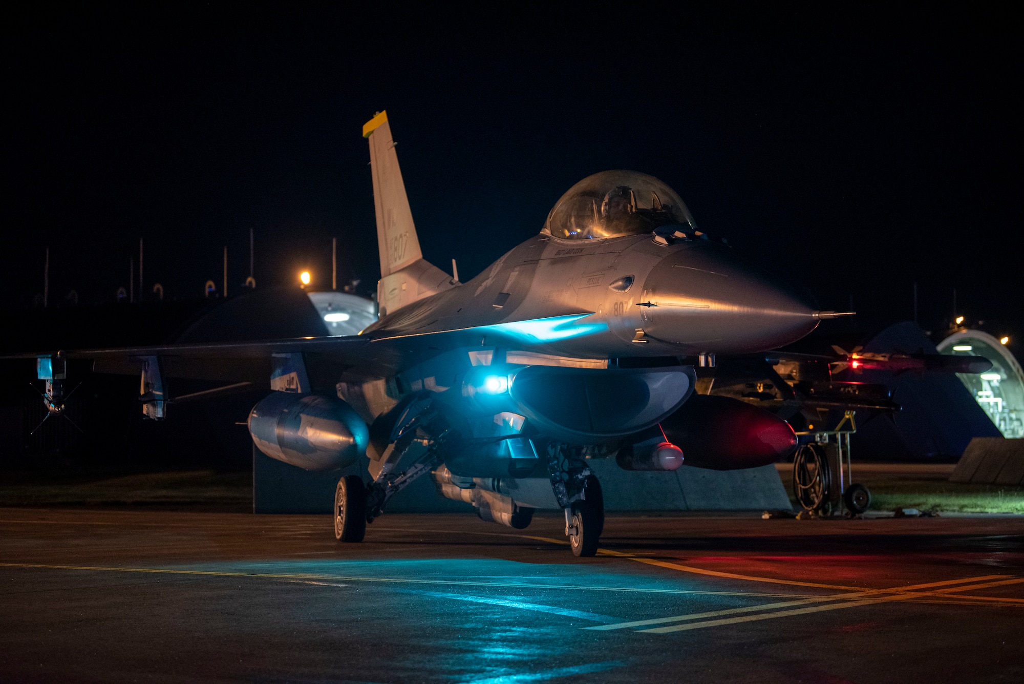 An F-16 Fighting Falcon sits on the runway at night.