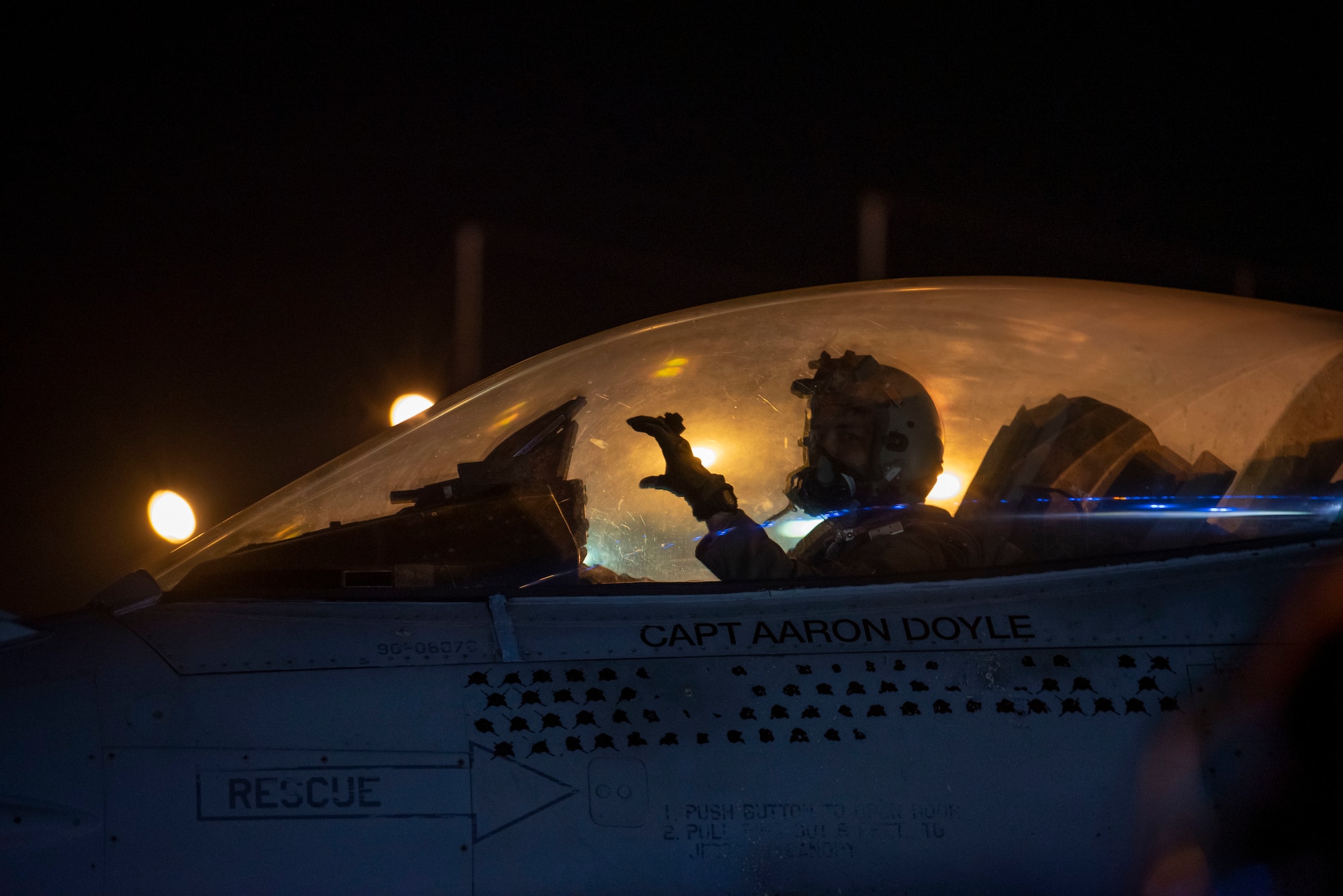 A pilot in the cockpit of an F-16 Fighting Falcon displays a hand gesture.