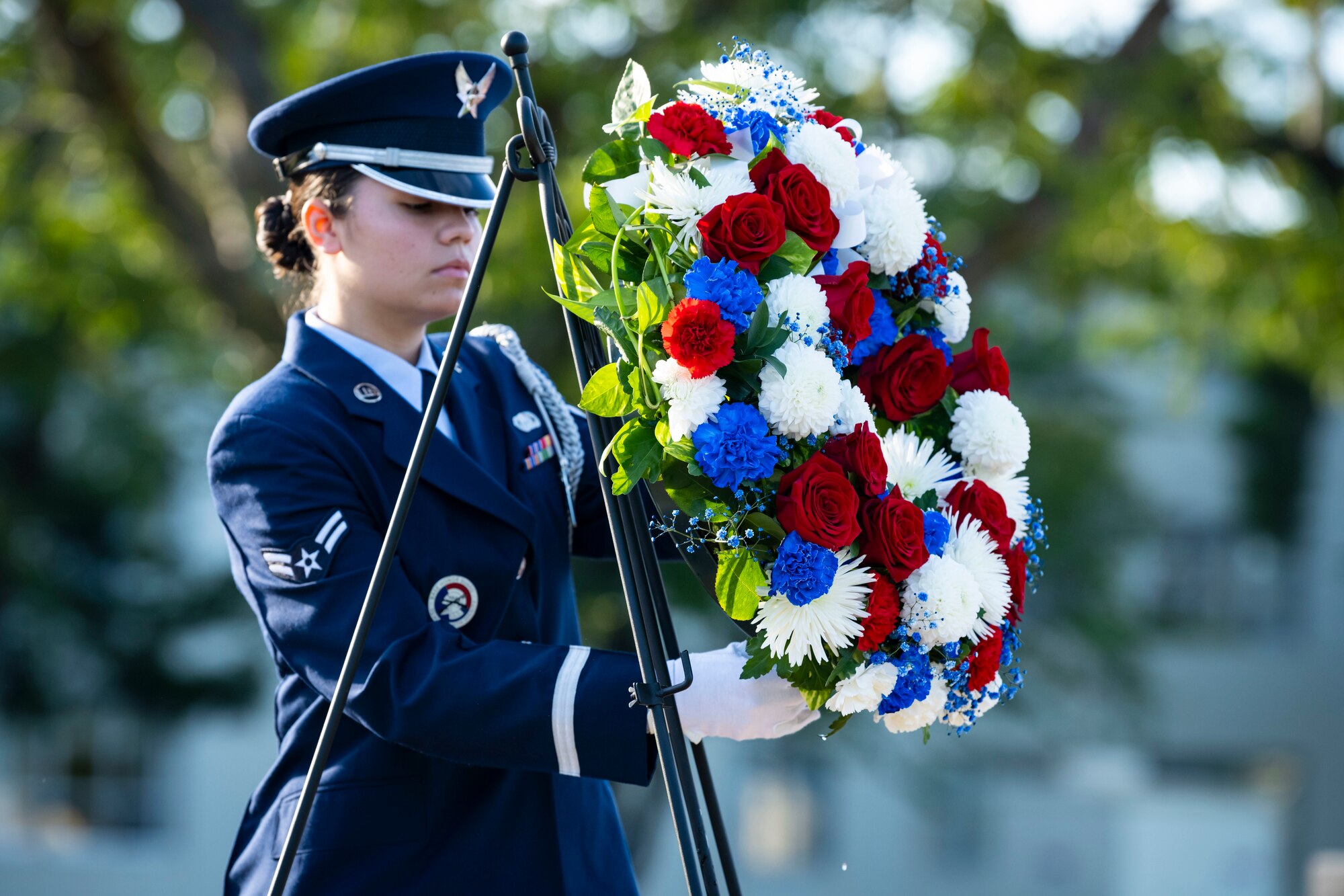 U.S. Air Force members in dress blues lifts a flower wreath off a stand.
