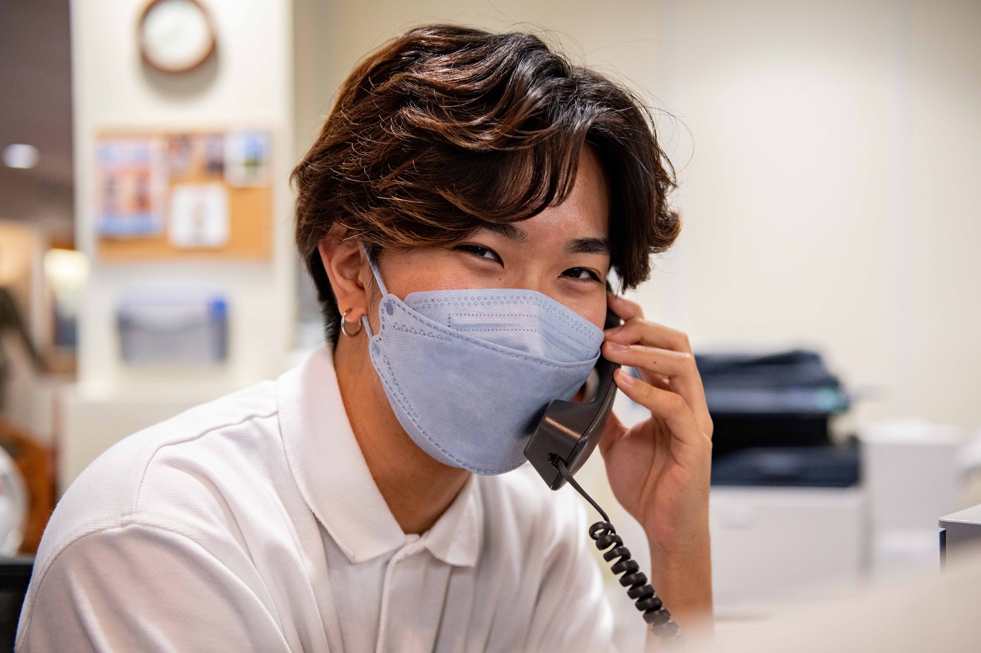A Japanese boy smiles at the camera as he takes a call at the front desk