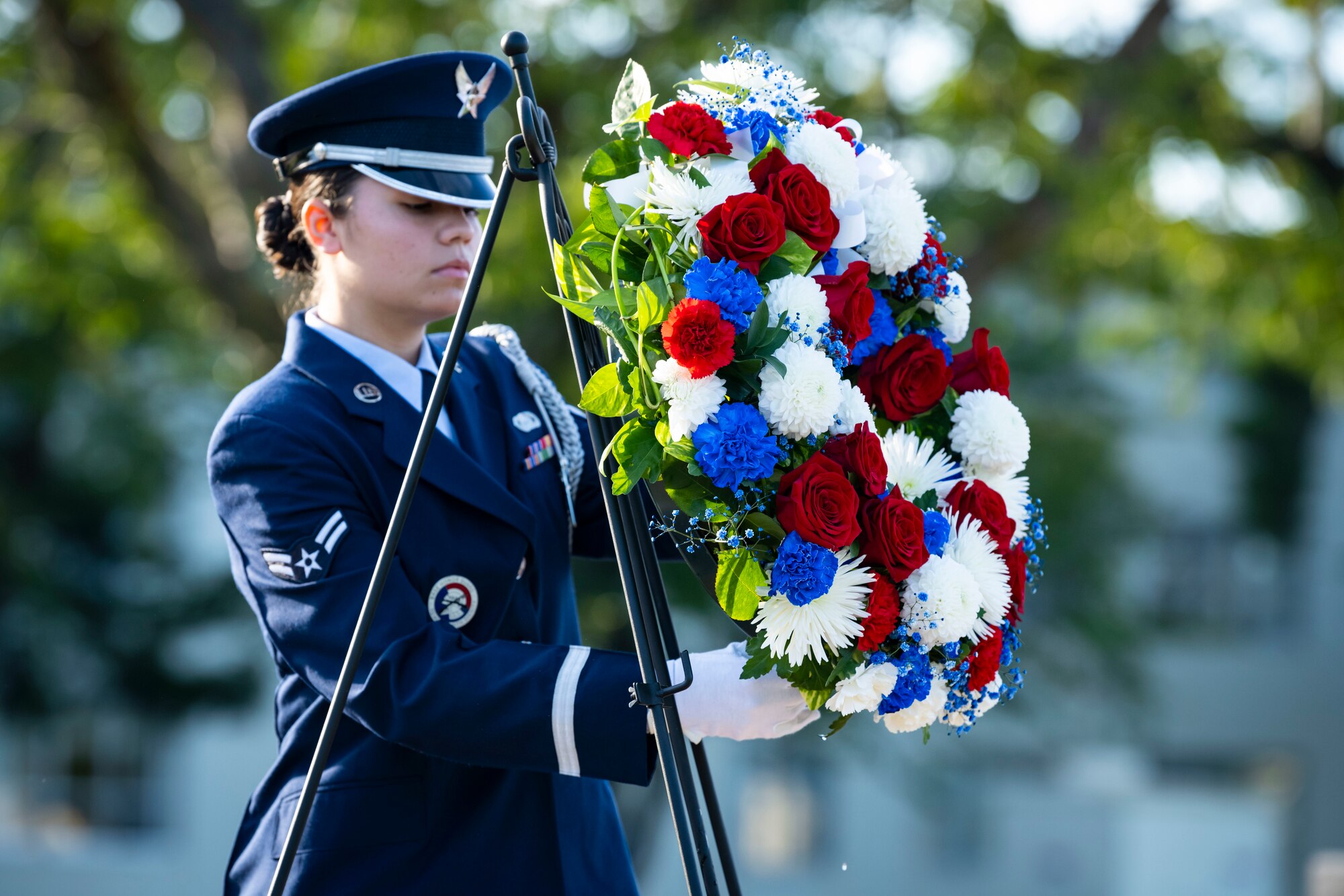 U.S. Air Force members in dress blues lifts a flower wreath off a stand.