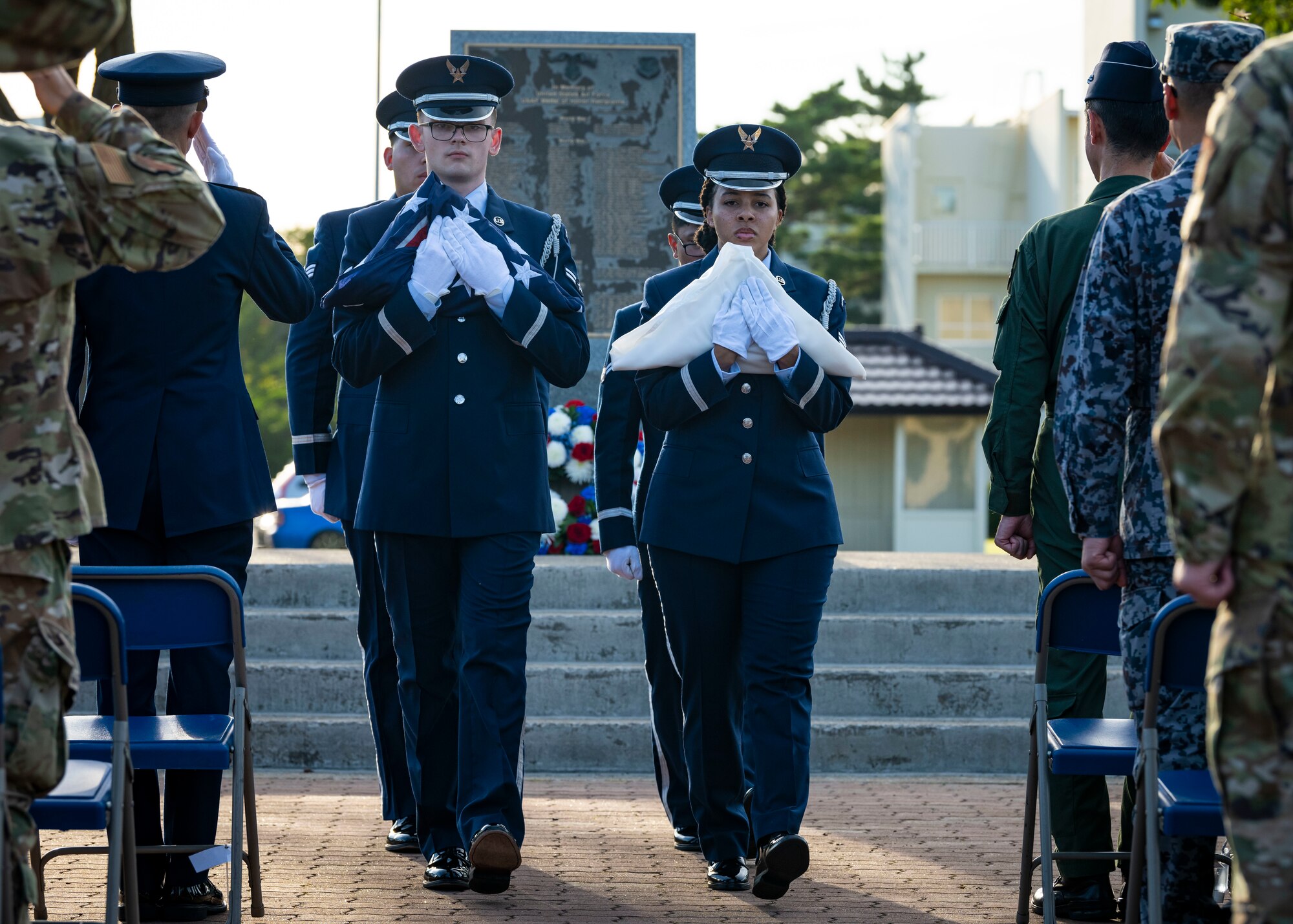 U.S. Air Force members in dress blues walk holding folded flags in their arms