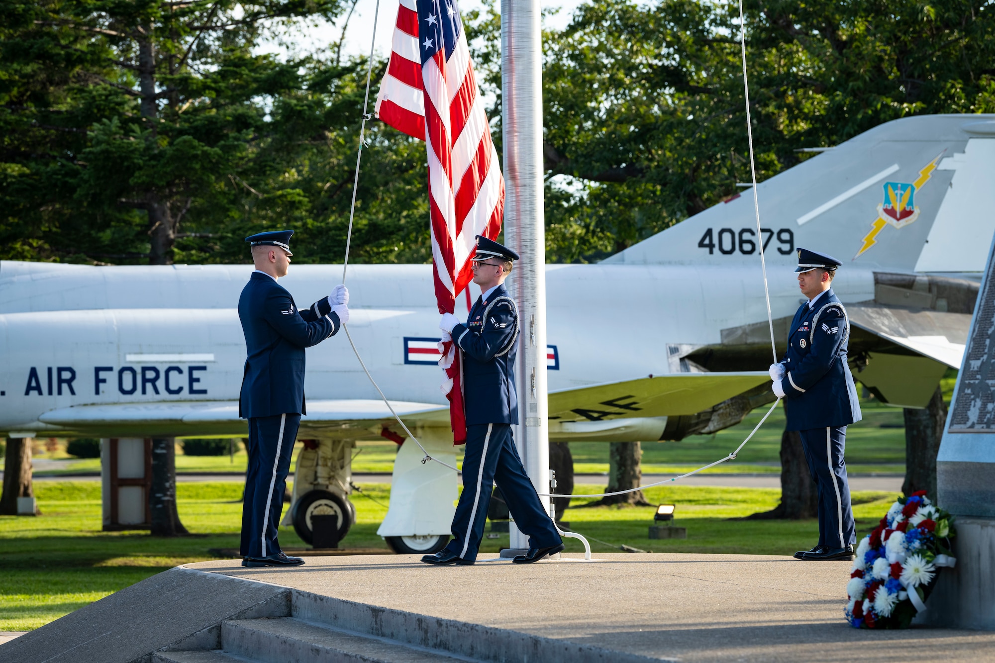 U.S. Air Force members in dress blues lower the U.S. flag off a pole.