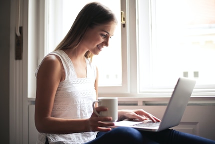 Woman browses her computer while holding a cup