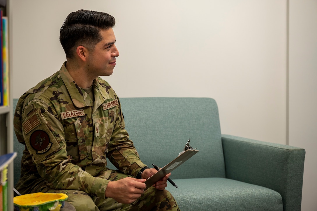 An airman sits on a couch holding a clipboard.