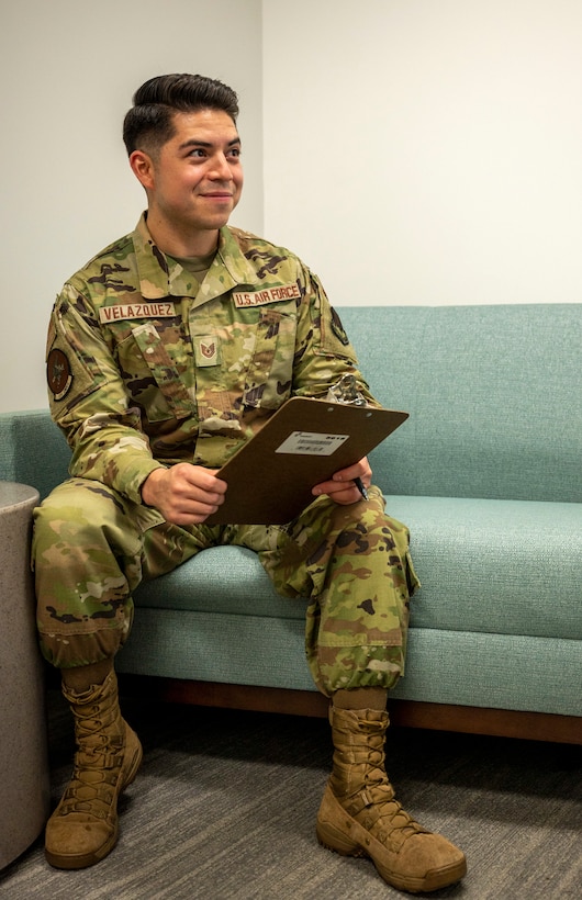 An airman sits on a couch with a clipboard.