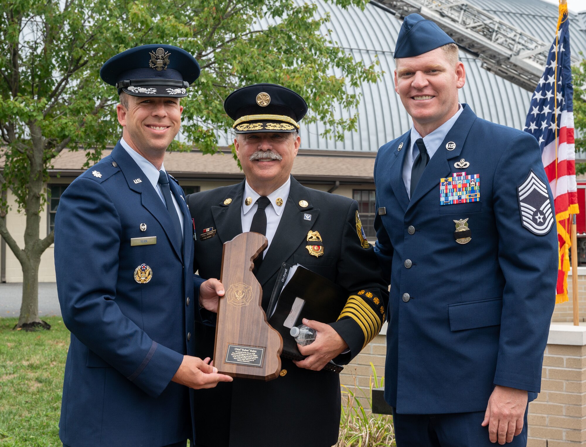 Lt. Col. Joshua Yerk, 436th Civil Engineer Squadron commander, left, and Chief Master Sgt. Andrew Kehl, 436th CES fire chief, right, present a plaque to Dennis Rubin, former Washington D.C. fire chief, during the 21st Anniversary 9/11 Memorial Ceremony held at the Air Mobility Command Museum on Dover Air Force Base, Delaware, Sept. 11, 2022. Rubin was the guest speaker during the ceremony which commemorated those who perished in the attacks on Sept. 11, 2001. (U.S. Air Force photo by Senior Airman Cydney Lee)