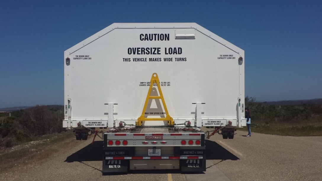 An oversized load of aerospace equipment is transported on a truck.