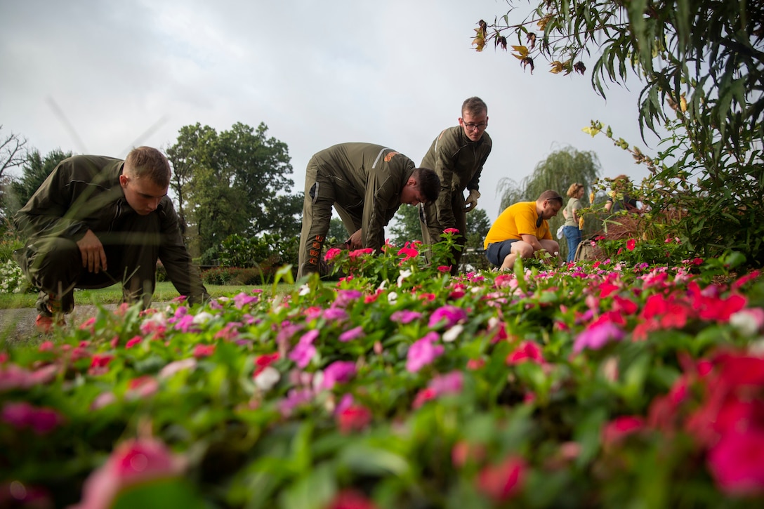 Marines and sailors work around a bed of flowers.