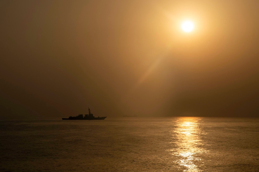 A ship transits a body of water under a sunlit sky.