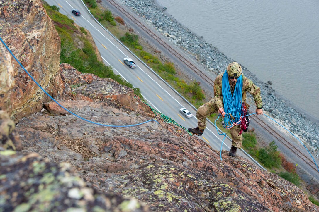 An airman climbs up a mountain; a roadway can be seen below.